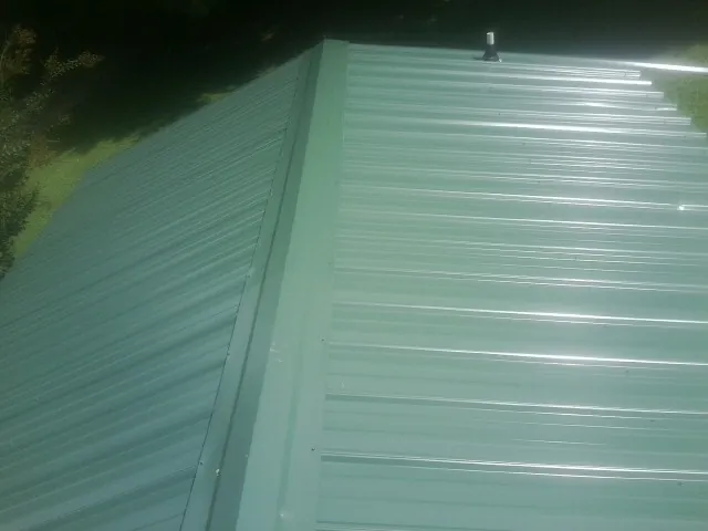 New green metal panels meeting at the ridge of a roof — Flat Roof Repair work by our crew in Hamersville