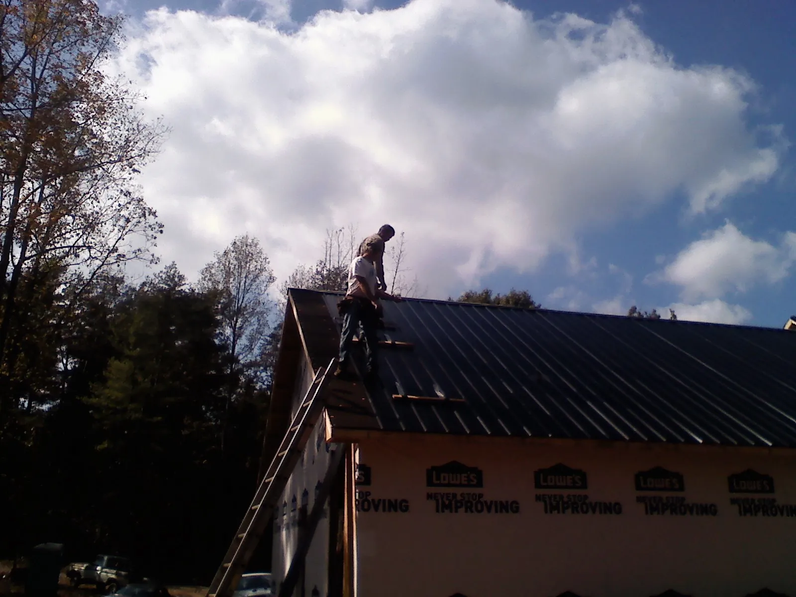 Roofer fastening dark metal panels high against a cloudy sky, from a Roof Inspection job in Hamersville