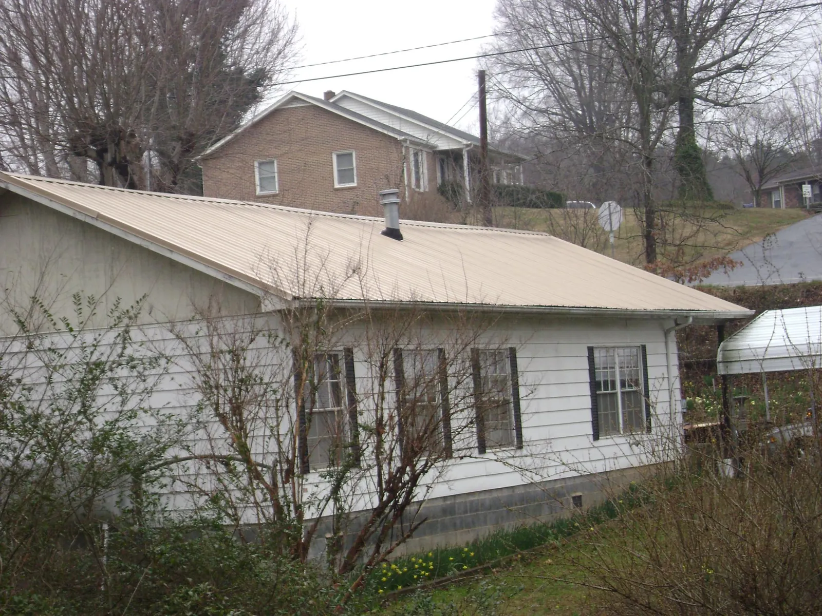 Tan metal roof on a white sided house set into a hillside — Commercial Roofing by Roofing Brothers in Hamersville