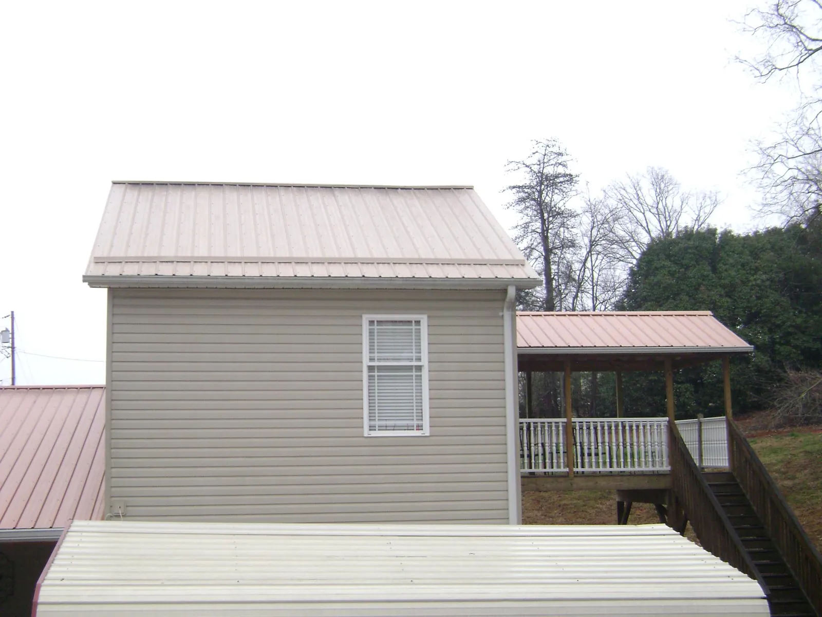 Tan metal roofs on a two story addition and attached porch, from a Roof Replacement job in Hamersville